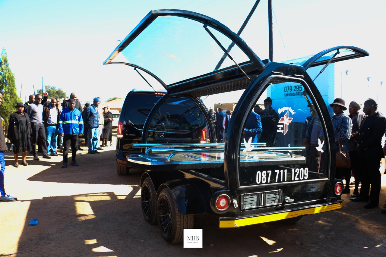 MHB glass carriage hearse trailer with open doors at a graveside service